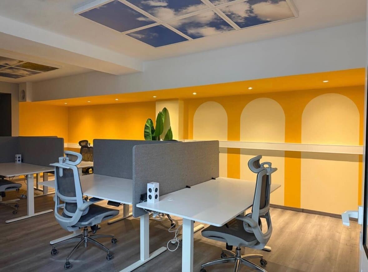 Open Space im CoWork Station Bakede – Coworking am Deister Open Space im Coworking Space CoWork Station Bakede: Arbeitsplätze mit höhenverstellbaren Tischen vor einer gelben Wand mit Rundbogennischen, Pflanzen und Himmeldecken-Panel